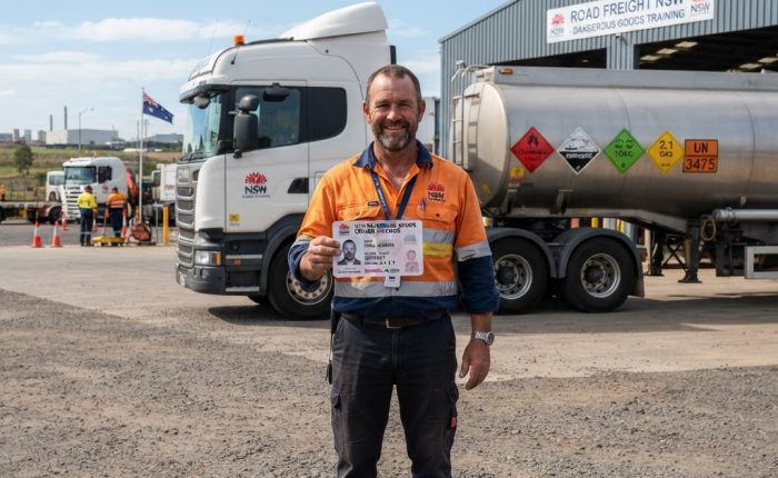 Truck driver holding dangerous goods licence card at NSW training facility with DG placard truck